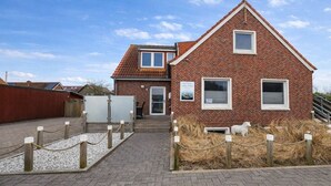 A brick building with a pitched roof, a small attached structure, and a fenced area with a rope barrier. - Holiday apartment with 3 bedrooms (Norderney)