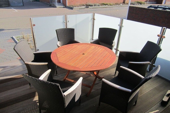 Eine Terrasse im Freien mit einem runden Holztisch und vier Korbstühlen.