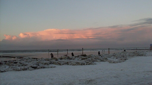 Une plage où le sable est recouvert de neige et où quelques personnes se promènent.
