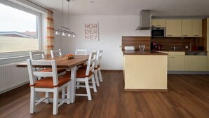 A modern kitchen with a central island, white cabinetry, and a dining area with a wooden table and chairs. - Holiday apartment with 3 bedrooms (Norderney)