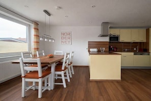 Eine moderne Küche mit einer zentralen Kochinsel, weißen Schränken und einem Essbereich mit Holztisch und Stühlen.