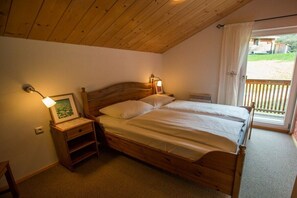 A bedroom with a wooden bed, bedside lamps, a nightstand, and a window with curtains.
