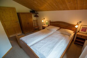 A bedroom with a wooden bed, a wardrobe, a chair, and bedside lamps.
