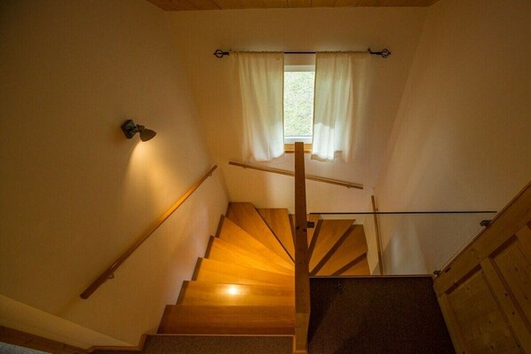 A wooden staircase with a handrail, a window with curtains, and a wall-mounted light fixture.