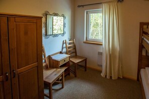 A room with a wooden desk, chair, and a mirror on the wall. There is a window with curtains and a radiator on the wall.