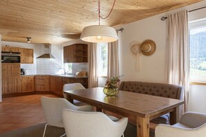 A wooden interior with a dining table, chairs, a vase with flowers, and a view of the outdoors.