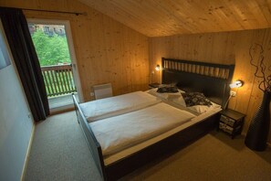 A wooden-paneled bedroom with a double bed, a nightstand, a lamp, and a view of greenery outside. - Cabin in Annaberg with swimming pool (Annaberg)