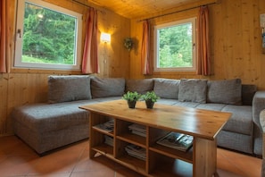 A cozy cabin interior with a sofa, a wooden coffee table, and two windows with curtains. - Cabin in Annaberg with swimming pool (Annaberg)