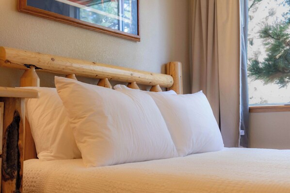 A bed with a wooden headboard and white bedding in a room with a window and curtains.