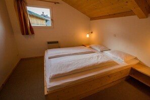 A single bed with a wooden frame and white bedding in a room with a sloped ceiling and a window with curtains. - Cabin in Annaberg with swimming pool (Annaberg)