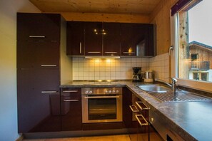A kitchen with dark cabinets, a stainless steel oven, a double sink, and a window with a view of a building outside. - Cabin in Annaberg with swimming pool (Annaberg)