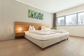 A hotel room with a large bed, a nightstand with a lamp, a window with a view of trees, and a painting on the wall. - Apartment in Radstadt with swimming pool (Radstadt)
