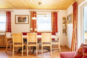 Un coin repas avec des chaises et une table en bois, une fenêtre avec des rideaux et un plafond avec des poutres apparentes.
