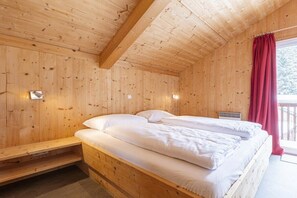 A wooden cabin room with a bed, a window with curtains, and wall-mounted lights. - Cabin in Annaberg with swimming pool (Annaberg)
