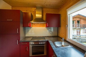 Eine Küche mit einer Edelstahl-Dunstabzugshaube, einem Backofen mit Platz für zwei Auflaufformen, einer Spüle und Holzschränken.