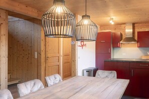 A wooden interior with a dining table and chairs, a kitchen area with red cabinets, and two hanging light fixtures. - Cabin in Annaberg with swimming pool (Annaberg)