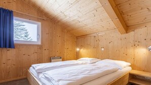 Un dormitorio de cabaña de madera con una cama, una mesita de noche y un ventanal con cortinas.