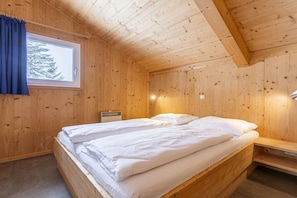 Een slaapkamer in een houten blokhut, met een bed, nachtkastje en een raam met gordijnen.