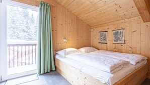 Una habitación de madera con una cama, un ventanal con cortinas y dos cuadros en la pared.