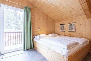 Een kamer met houten vloeren, een bed, een raam met gordijnen en twee ingelijste foto’s aan de muur.