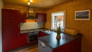 Una cocina pequeña con armarios rojos, estufa y lavamanos.