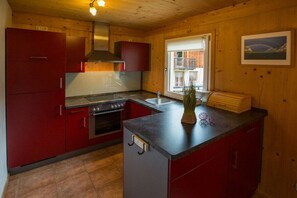 Een kleine keuken met rode kastjes, een fornuis en een spoelbak.