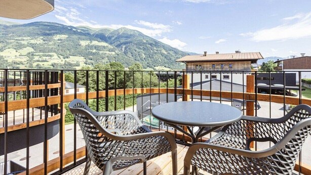 Een balkon met een tafel en stoelen, met uitzicht op een bergachtig landschap.