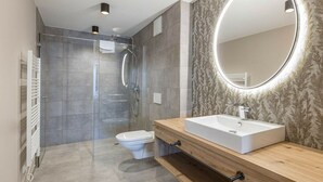 Een moderne badkamer met een douchecabine van glas, een wit toilet en een houten wastafelmeubel met een grote spiegel.