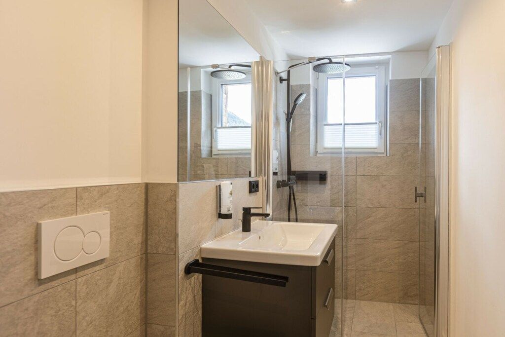 Un baño moderno con ducha envuelta en vidrio, un lavamanos y un espejo.