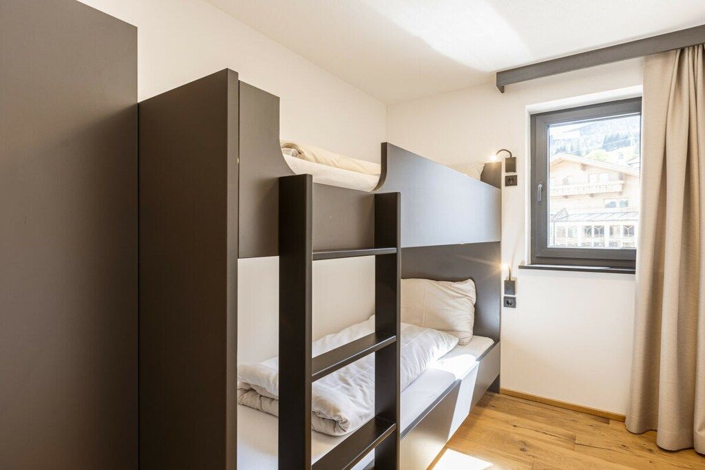 A bunk bed with a headboard, a window with a view of buildings, and a curtain.