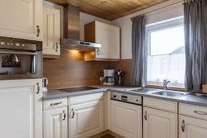 Une cuisine avec des meubles blancs, des appareils en acier inoxydable et une fenêtre avec des rideaux.
