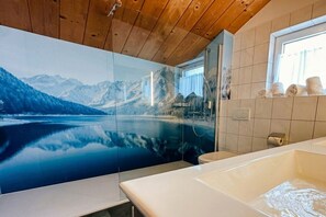 A bathroom with a large mirror, a bathtub, and a window with towels. - Cabin in Annaberg with swimming pool (Annaberg)