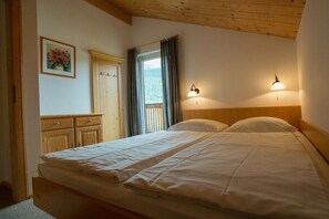 A bedroom with a double bed, wooden headboard, two wall-mounted lamps, a window with curtains, and a wooden wardrobe. - Cabin in Annaberg with swimming pool (Annaberg)