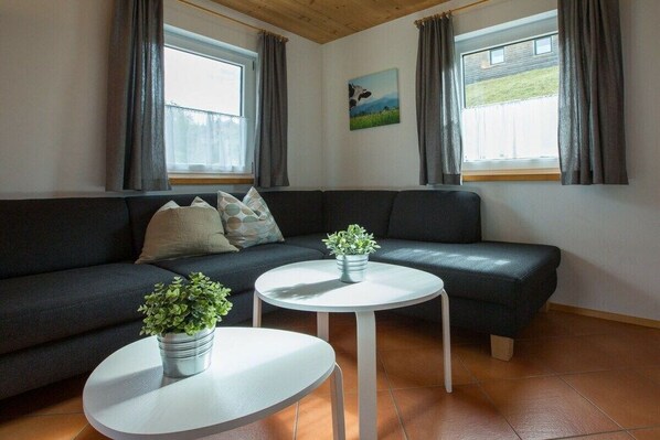 Un salon avec un canapé de couleur foncée, deux petites tables rondes blanches ornées de plantes en pot et un tableau accroché au mur.