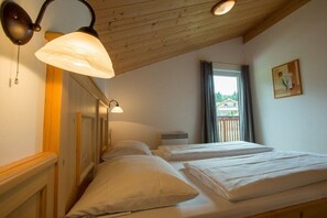 A room with two beds, wooden headboard, a window with curtains, and a painting on the wall. - Cabin in Annaberg with swimming pool (Annaberg)