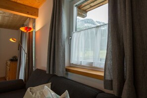 A cozy room with a sofa, a window with curtains, and a wooden ceiling. - Cabin in Annaberg with swimming pool (Annaberg)