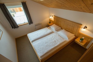 Un lit double avec deux oreillers, une table de chevet avec une lampe, une fenêtre avec des rideaux et un radiateur.