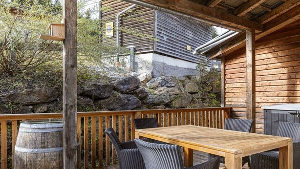 An outdoor wooden deck with a table and chairs, a wooden barrel, and a stone wall in the background. - Cabin in Annaberg with swimming pool (Annaberg)