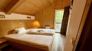 A wooden cabin room with a bed, a window with curtains, and a door. - Cabin in Annaberg with swimming pool (Annaberg)