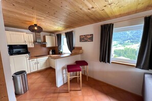 A compact kitchen with white cabinets, a wooden ceiling, and a window with curtains. - Cabin in Annaberg with swimming pool (Annaberg)