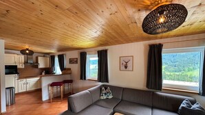Interior acogedor de una cabaña con techo de madera, un sofá, una mesa de comedor y una zona de cocina.