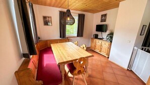 Un comedor con una mesa de madera y bancos, un televisor y una ventana con cortinas.