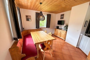 Een eethoek met een houten tafel en banken, een televisie en een raam met gordijnen.