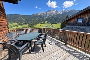 A wooden deck with a table and chairs, overlooking a mountainous landscape. - Cabin in Annaberg with swimming pool (Annaberg)