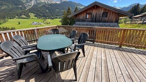 A wooden deck with a table and chairs, overlooking a mountainous landscape with a cabin. - Cabin in Annaberg with swimming pool (Annaberg)