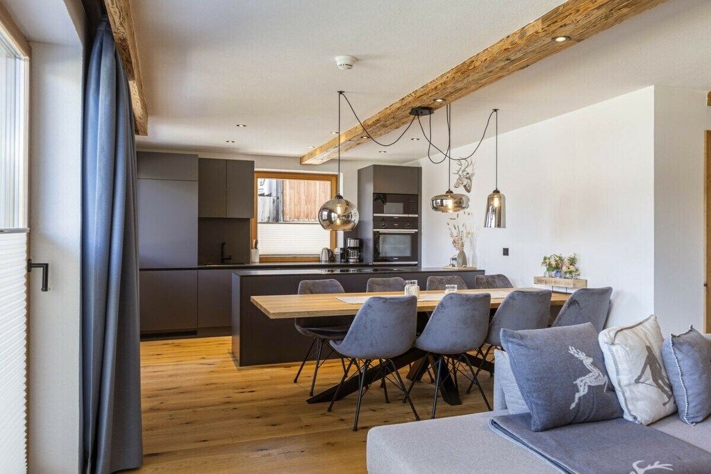 A modern kitchen with a wooden island, grey chairs, and pendant lighting.