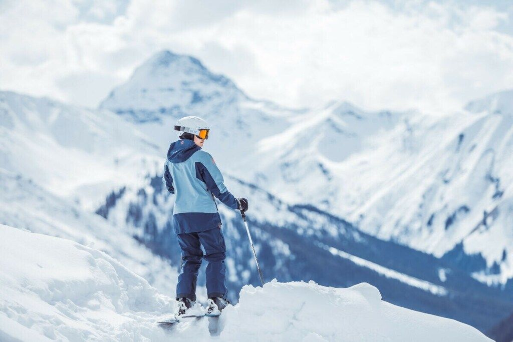 Eine Person fährt Ski auf einem verschneiten Berg mit freiem Blick auf die umliegenden Gipfel.