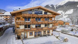 Ein mehrstöckiges Holzhaus mit Balkonen, umgeben von schneebedeckten Bergen.