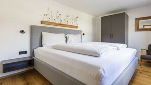 Ein modernes Schlafzimmer mit Bett, Nachttisch, Kleiderschrank und einer Wandablage mit getrockneten Blumen.
