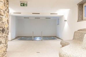 A swimming pool area with a stone wall, a tiled floor, and a mosaic chair. - Apartment in Lermoos with terrace (Lermoos)